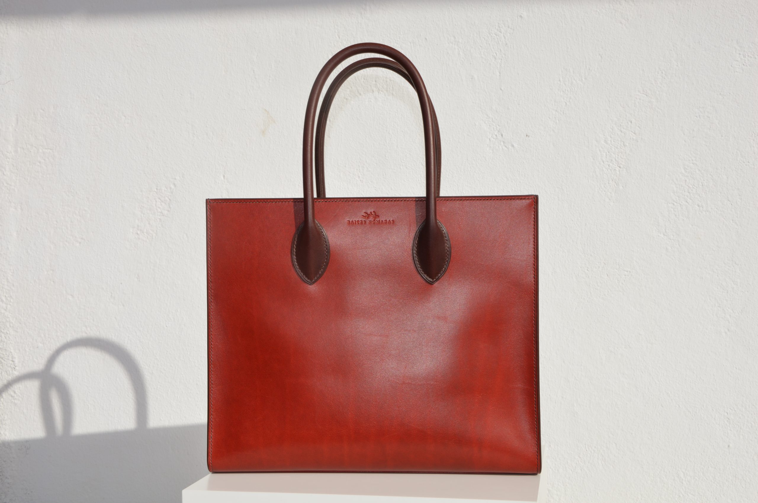 "Tote Bag con cremallera disponible por €1,400.00. Este clásico bolso combina belleza atemporal y líneas armónicas. Creado con el máximo cuidado, está confeccionado con la mejor piel de curtido vegetal española, hilos de lino y cosido completamente a mano. El bolso artesanal presenta un elegante color cereza con asas color tabaco, y está forrado con piel de cabra francesa. Cuenta con un bolsillo interior sin cremallera y otro con cremallera, además de un cierre exterior. Cada detalle de este bolso refleja la artesanía y la calidad de su fabricación, 100% cosido a mano."