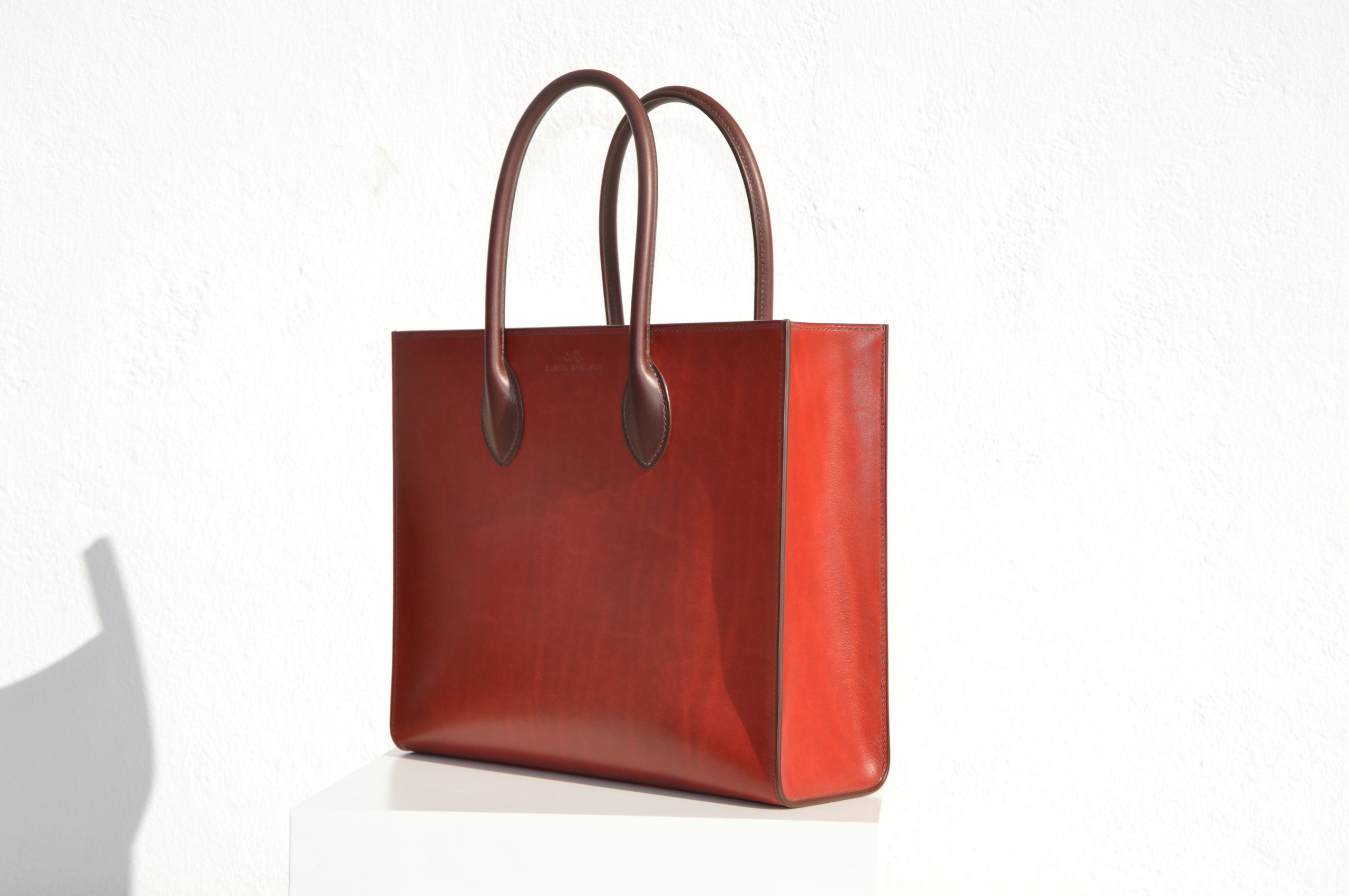 "Tote Bag con cremallera disponible por €1,400.00. Este clásico bolso combina belleza atemporal y líneas armónicas. Creado con el máximo cuidado, está confeccionado con la mejor piel de curtido vegetal española, hilos de lino y cosido completamente a mano. El bolso artesanal presenta un elegante color cereza con asas color tabaco, y está forrado con piel de cabra francesa. Cuenta con un bolsillo interior sin cremallera y otro con cremallera, además de un cierre exterior. Cada detalle de este bolso refleja la artesanía y la calidad de su fabricación, 100% cosido a mano."