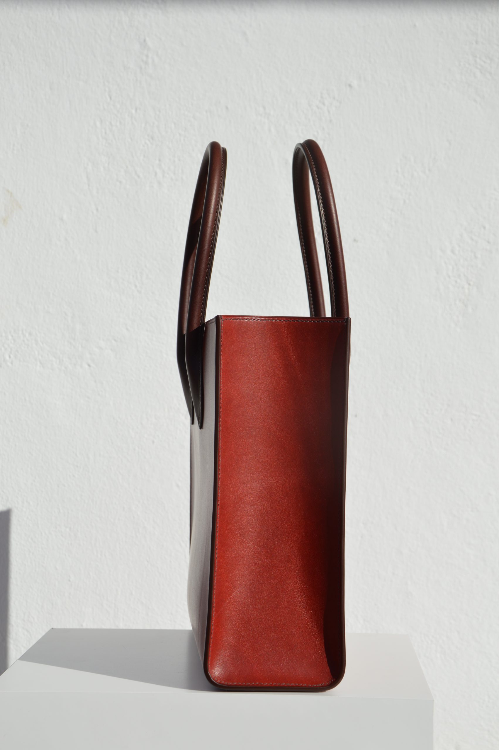 "Tote Bag con cremallera disponible por €1,400.00. Este clásico bolso combina belleza atemporal y líneas armónicas. Creado con el máximo cuidado, está confeccionado con la mejor piel de curtido vegetal española, hilos de lino y cosido completamente a mano. El bolso artesanal presenta un elegante color cereza con asas color tabaco, y está forrado con piel de cabra francesa. Cuenta con un bolsillo interior sin cremallera y otro con cremallera, además de un cierre exterior. Cada detalle de este bolso refleja la artesanía y la calidad de su fabricación, 100% cosido a mano."