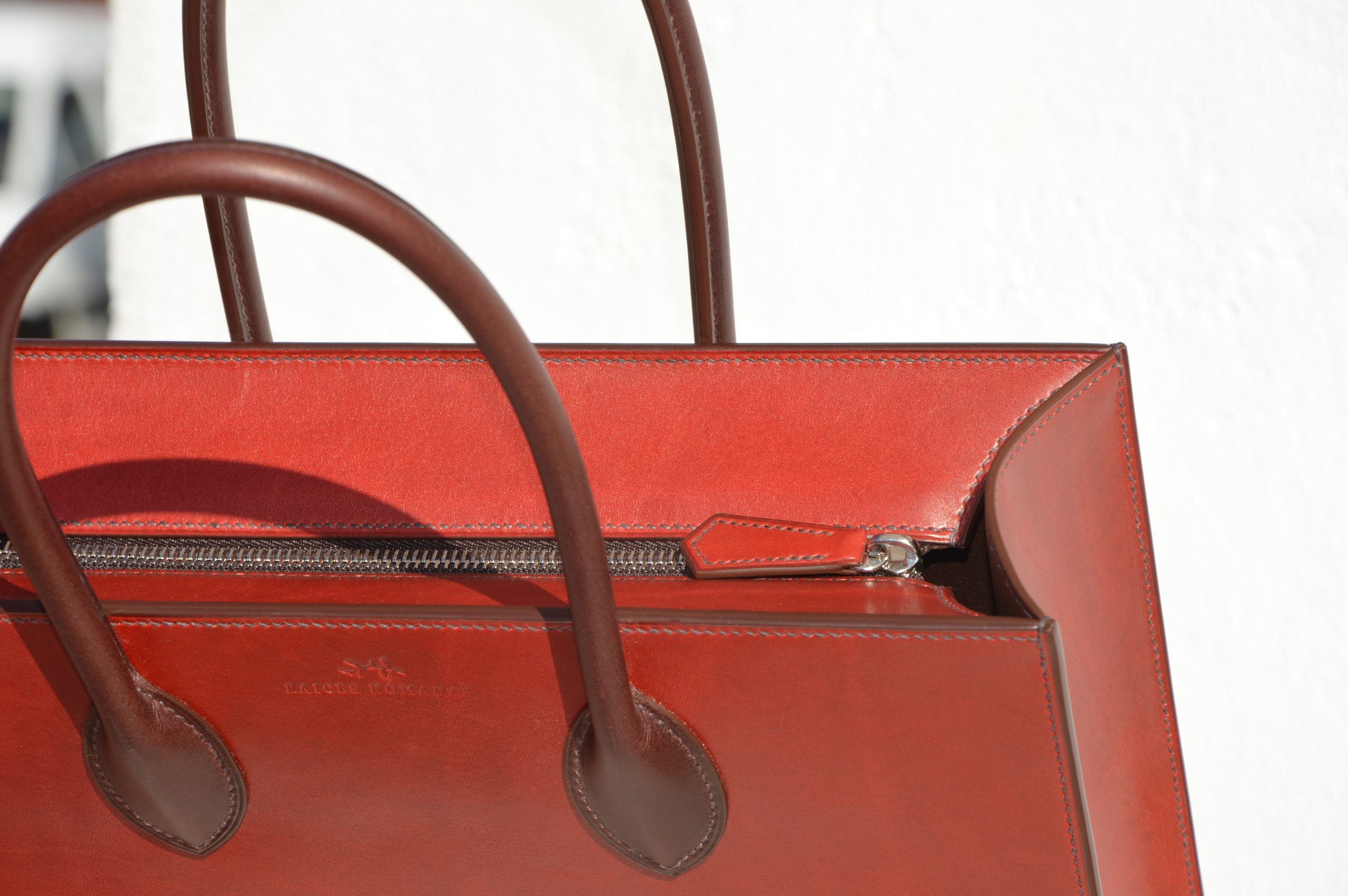 "Tote Bag con cremallera disponible por €1,400.00. Este clásico bolso combina belleza atemporal y líneas armónicas. Creado con el máximo cuidado, está confeccionado con la mejor piel de curtido vegetal española, hilos de lino y cosido completamente a mano. El bolso artesanal presenta un elegante color cereza con asas color tabaco, y está forrado con piel de cabra francesa. Cuenta con un bolsillo interior sin cremallera y otro con cremallera, además de un cierre exterior. Cada detalle de este bolso refleja la artesanía y la calidad de su fabricación, 100% cosido a mano."