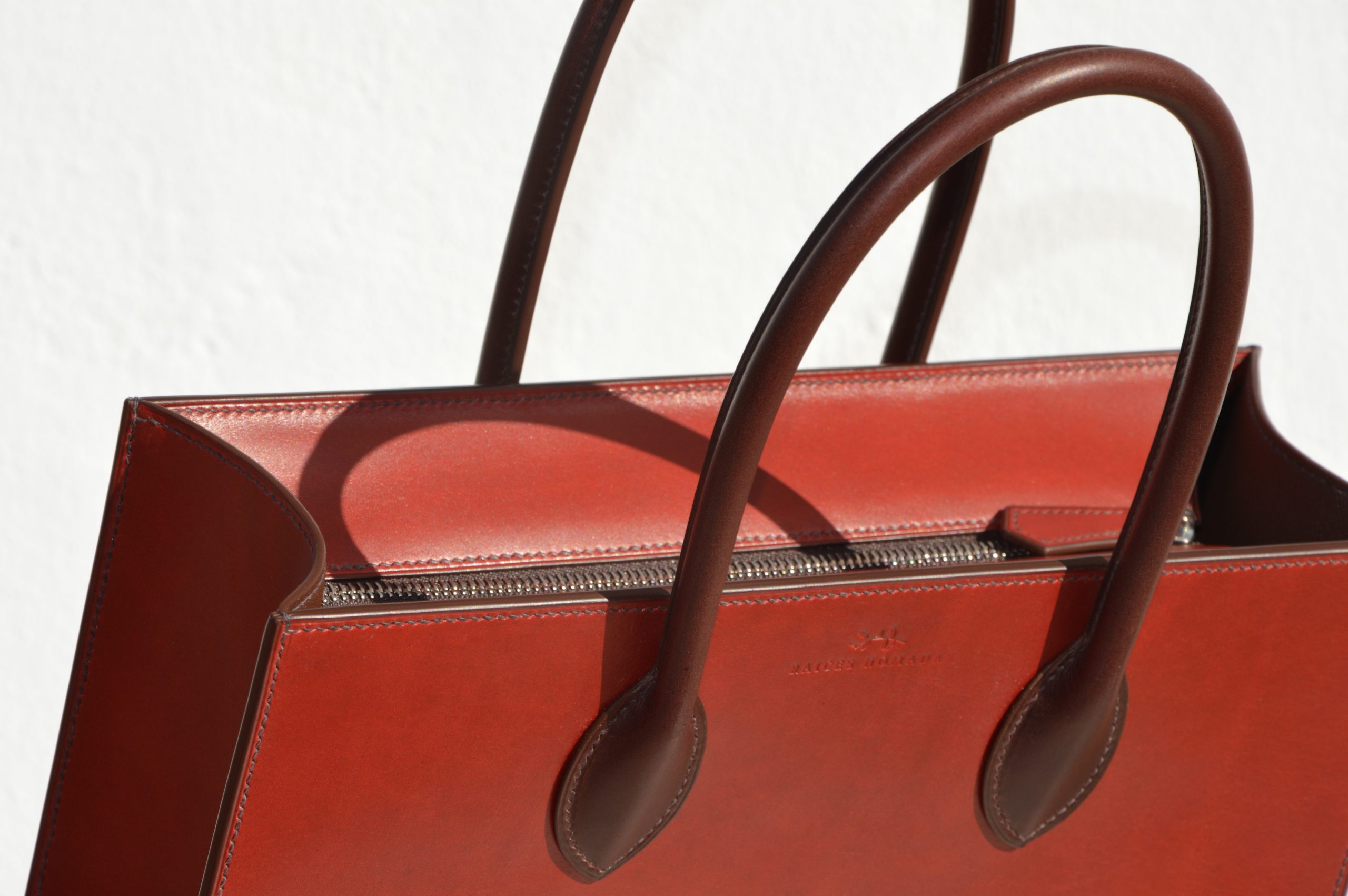 "Tote Bag con cremallera disponible por €1,400.00. Este clásico bolso combina belleza atemporal y líneas armónicas. Creado con el máximo cuidado, está confeccionado con la mejor piel de curtido vegetal española, hilos de lino y cosido completamente a mano. El bolso artesanal presenta un elegante color cereza con asas color tabaco, y está forrado con piel de cabra francesa. Cuenta con un bolsillo interior sin cremallera y otro con cremallera, además de un cierre exterior. Cada detalle de este bolso refleja la artesanía y la calidad de su fabricación, 100% cosido a mano."