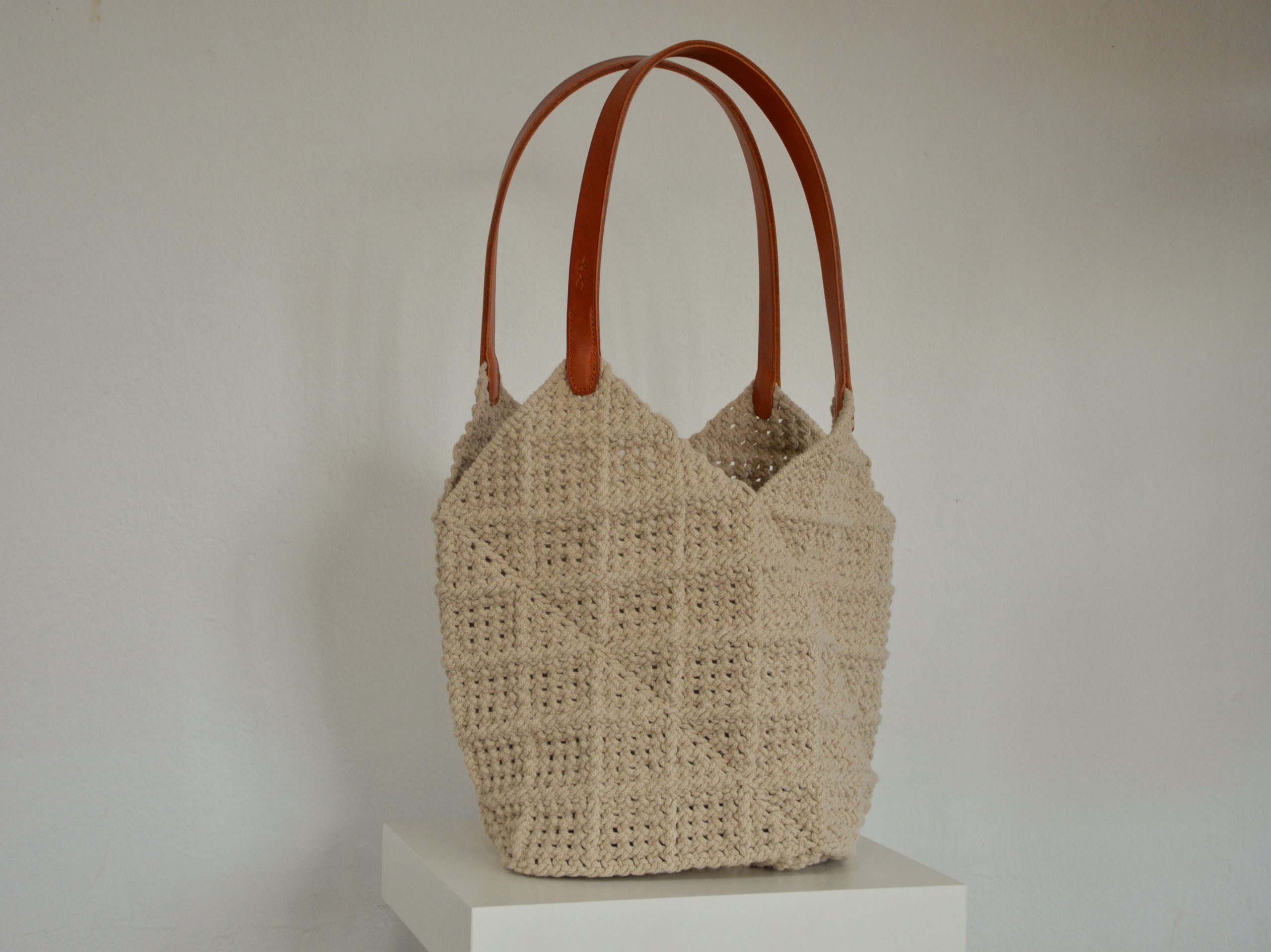 "'Windmill Bag' disponible por €350.00. Esta amplia bolsa artesanal está realizada en macramé con cuerdas de algodón sostenible certificado por OEKO-TEX, con asas de piel de curtido vegetal en color sol. Cada detalle de esta bolsa, desde las técnicas de macramé hasta las asas cosidas a mano con hilos de lino, refleja la artesanía y la calidad de los materiales utilizados."