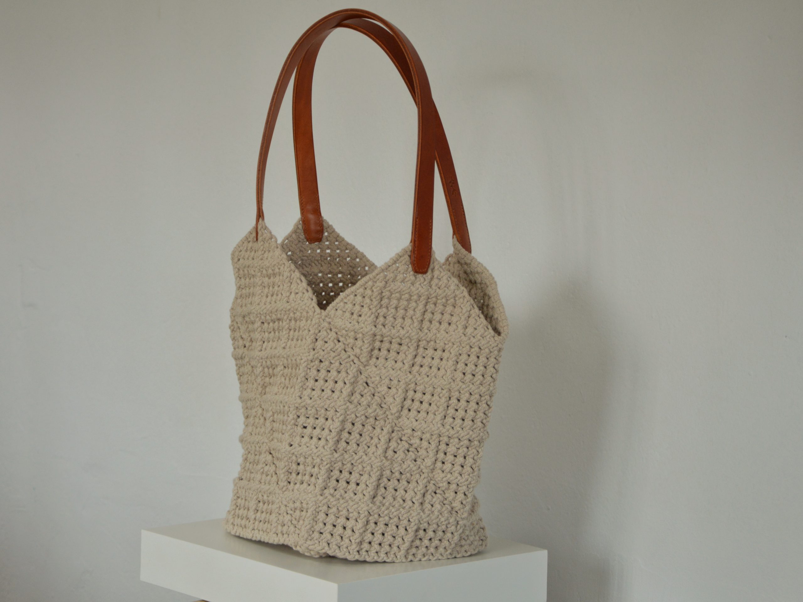 "'Windmill Bag' disponible por €350.00. Esta amplia bolsa artesanal está realizada en macramé con cuerdas de algodón sostenible certificado por OEKO-TEX, con asas de piel de curtido vegetal en color sol. Cada detalle de esta bolsa, desde las técnicas de macramé hasta las asas cosidas a mano con hilos de lino, refleja la artesanía y la calidad de los materiales utilizados."