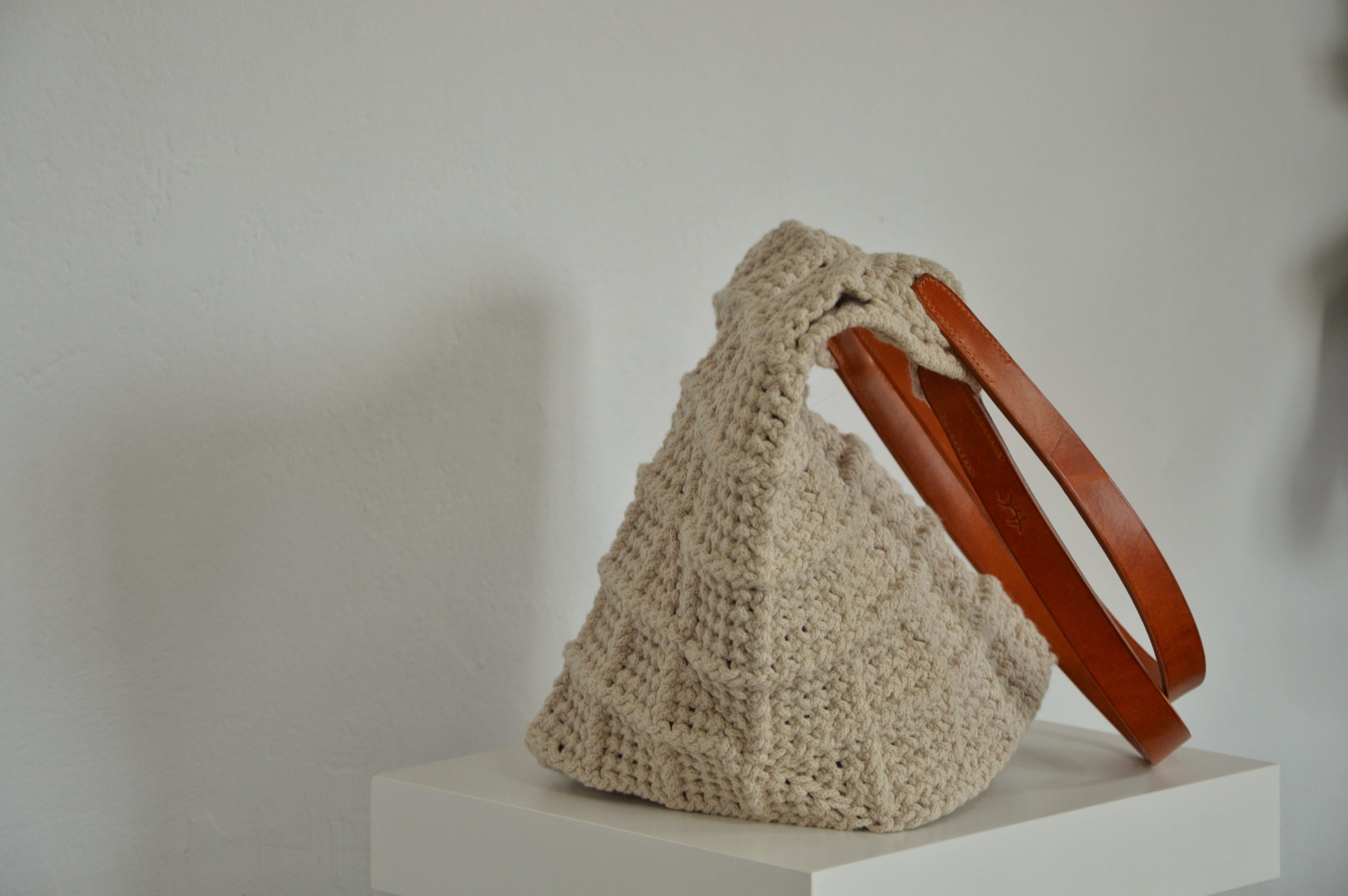 "'Windmill Bag' disponible por €350.00. Esta amplia bolsa artesanal está realizada en macramé con cuerdas de algodón sostenible certificado por OEKO-TEX, con asas de piel de curtido vegetal en color sol. Cada detalle de esta bolsa, desde las técnicas de macramé hasta las asas cosidas a mano con hilos de lino, refleja la artesanía y la calidad de los materiales utilizados."
