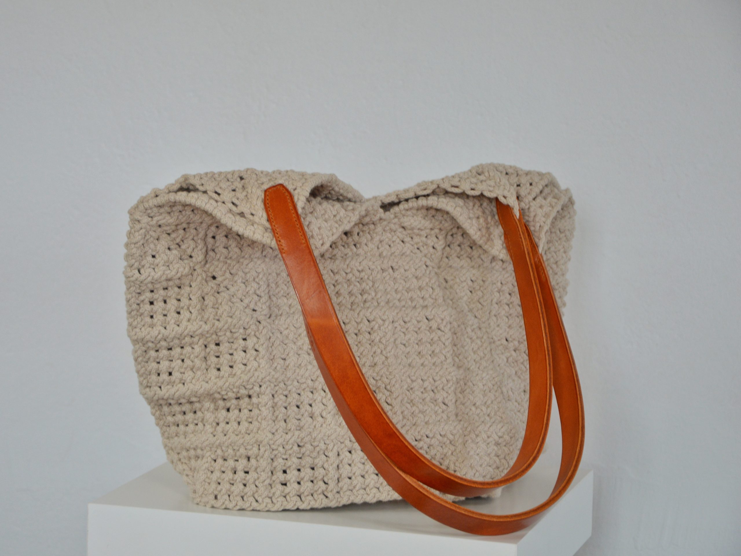 "'Windmill Bag' disponible por €350.00. Esta amplia bolsa artesanal está realizada en macramé con cuerdas de algodón sostenible certificado por OEKO-TEX, con asas de piel de curtido vegetal en color sol. Cada detalle de esta bolsa, desde las técnicas de macramé hasta las asas cosidas a mano con hilos de lino, refleja la artesanía y la calidad de los materiales utilizados."