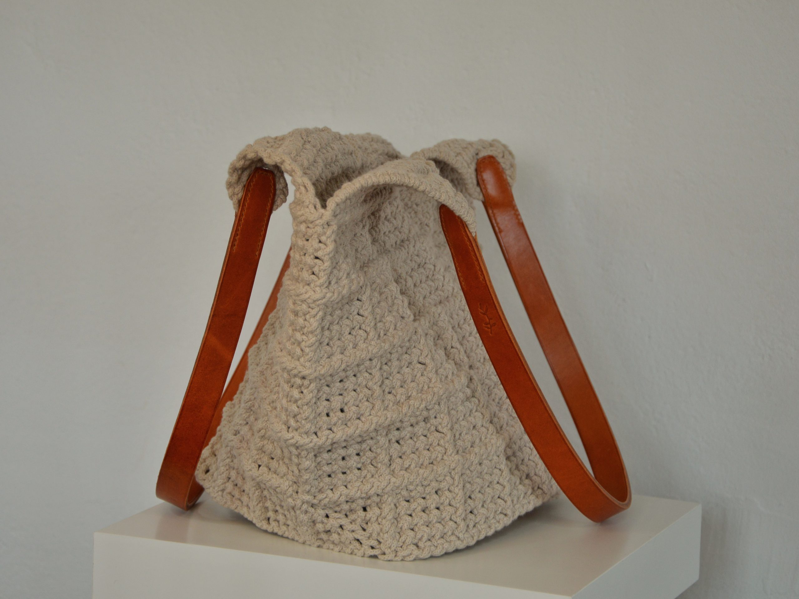 "'Windmill Bag' disponible por €350.00. Esta amplia bolsa artesanal está realizada en macramé con cuerdas de algodón sostenible certificado por OEKO-TEX, con asas de piel de curtido vegetal en color sol. Cada detalle de esta bolsa, desde las técnicas de macramé hasta las asas cosidas a mano con hilos de lino, refleja la artesanía y la calidad de los materiales utilizados."