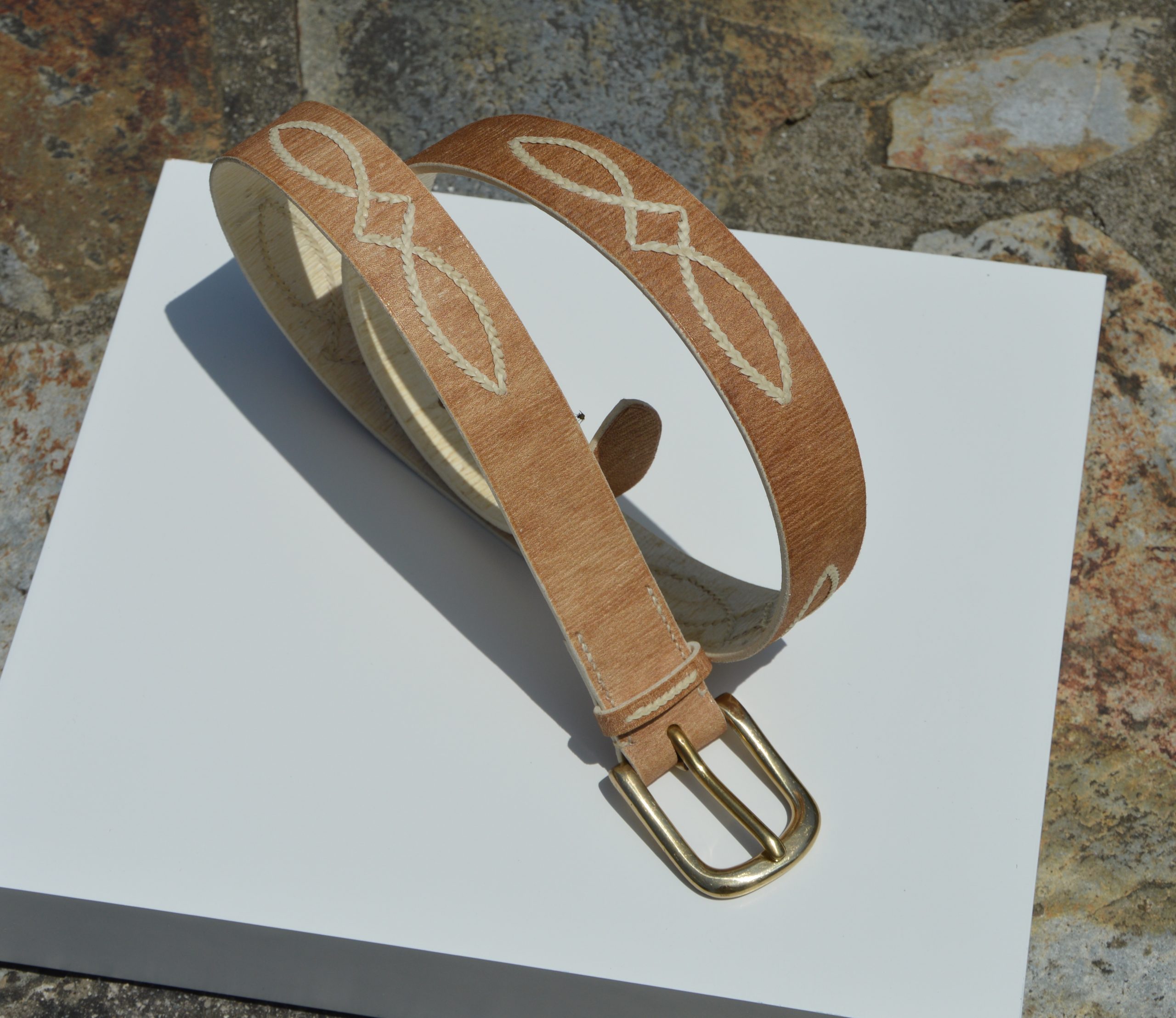 "Cinturón de Cuero Ojo de Perdiz disponible por €150.00. Elaborado con las técnicas y materiales típicos de la artesanía criolla, este cinturón presenta cuero crudo con costuras decorativas de tiento y una hebilla de latón macizo. Puedes consultarnos por más opciones de diseño. Disponible en 30 mm o 35 mm de ancho."