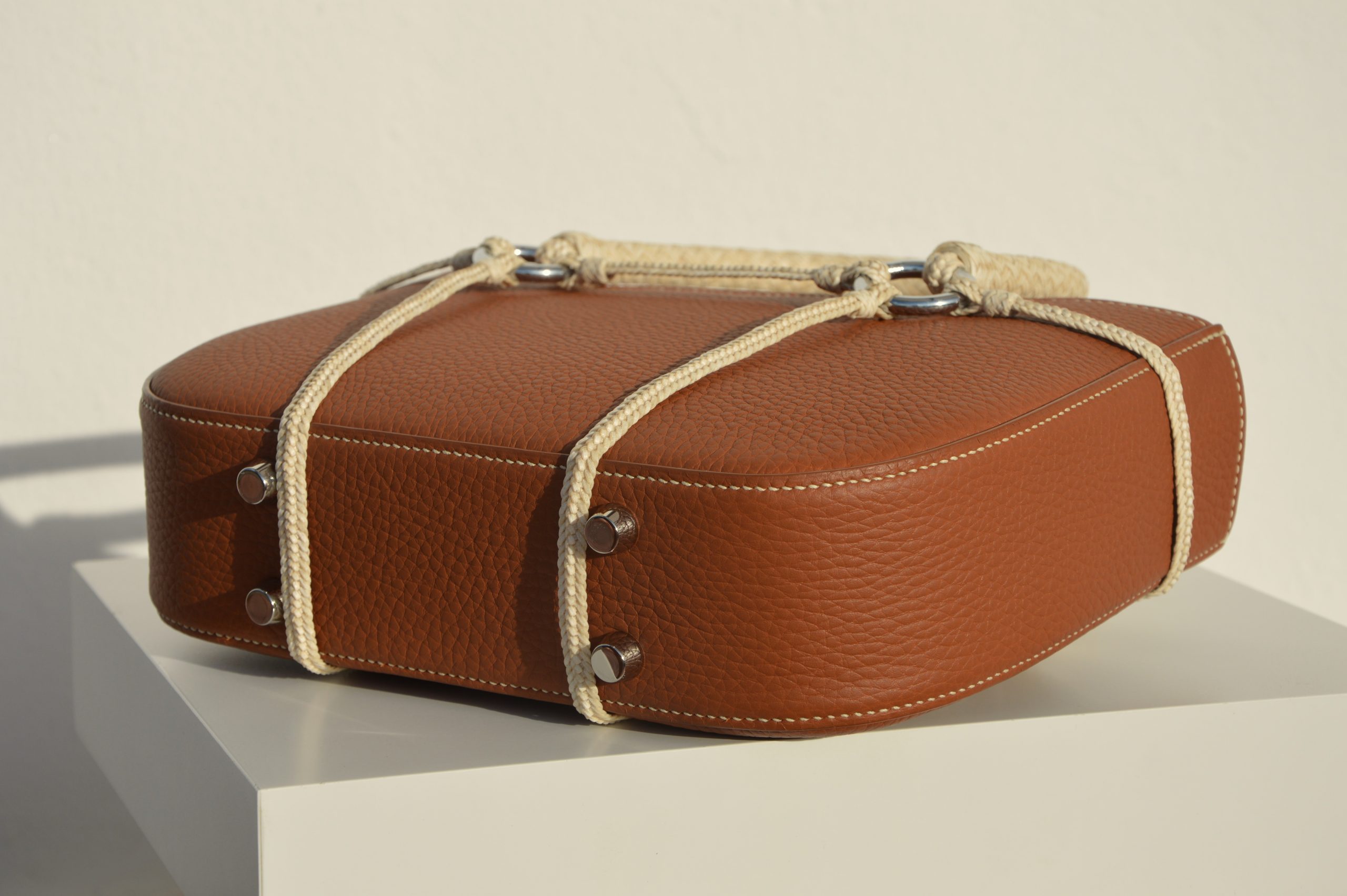 "Bolso Tobiano de edición limitada, elaborado en piel Taurillon Lagun con asas tejidas a lezna y arnés trenzado en cuero crudo. Forrado en piel de cabra francesa y cosido a mano con hilos de lino. Dimensiones: 6cm x 25cm x 30cm, incluyendo asas."